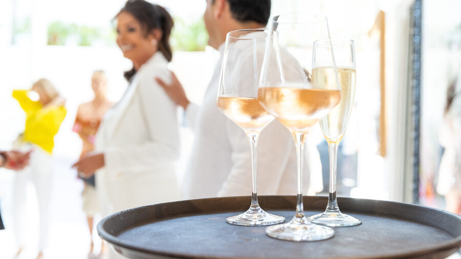 Three glasses of rosé on a tray. Guests in the background.